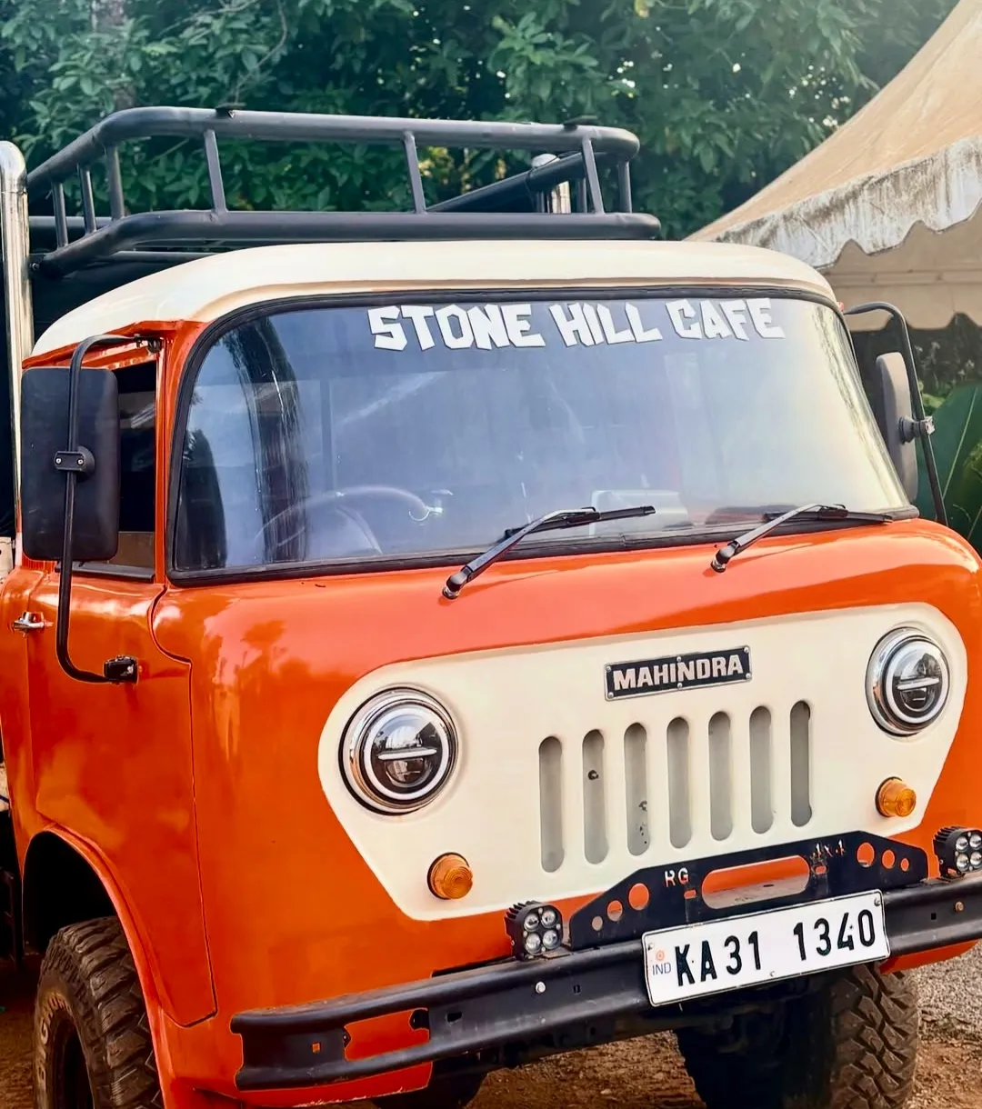 An orange Mahindra jeep parked on the property, "Stone Hill Cafe" lettered across its windscreen.