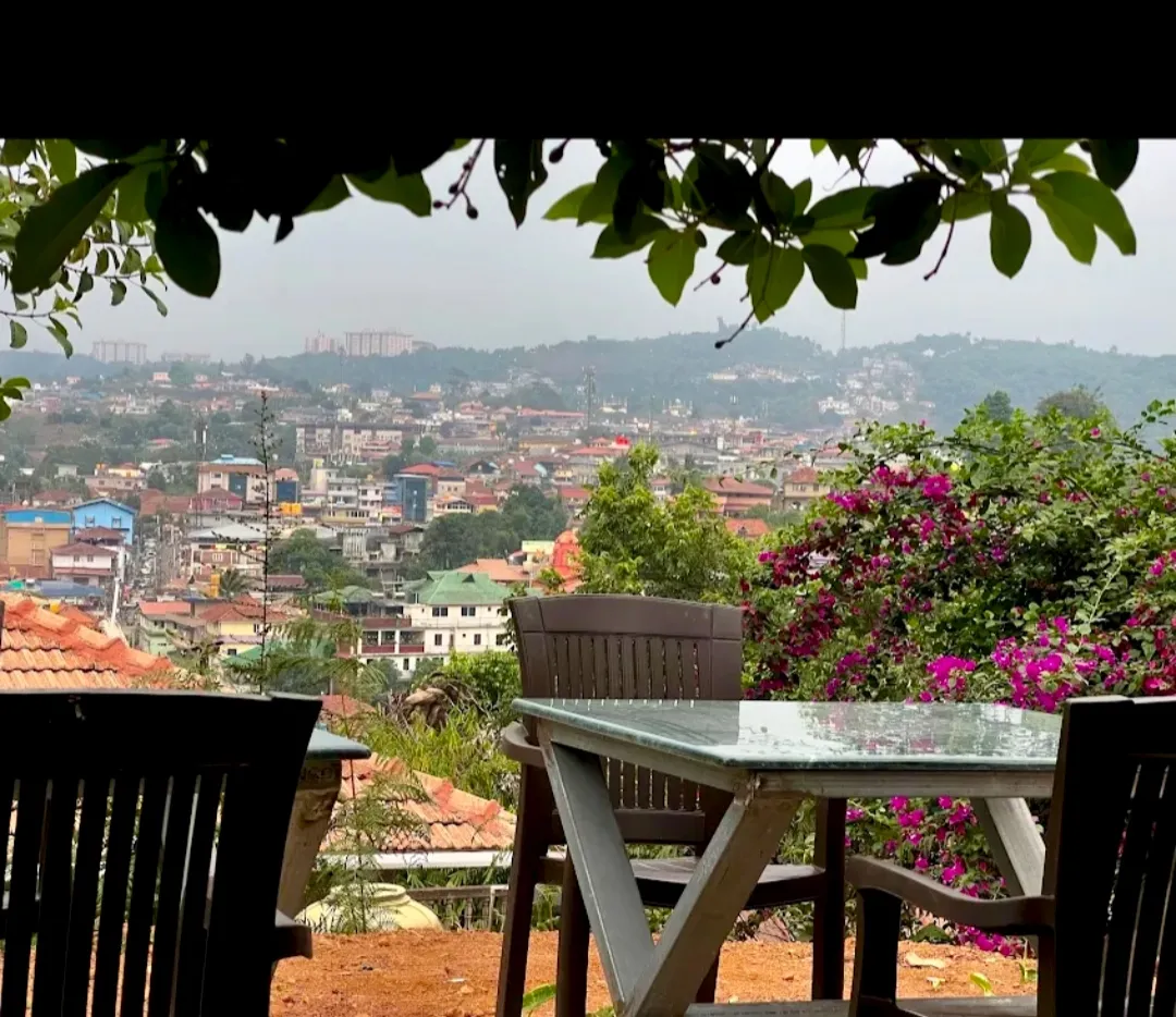 A wooden table on the terrace under flowering bougainvillea, looking out over the rooftops of Madikeri.