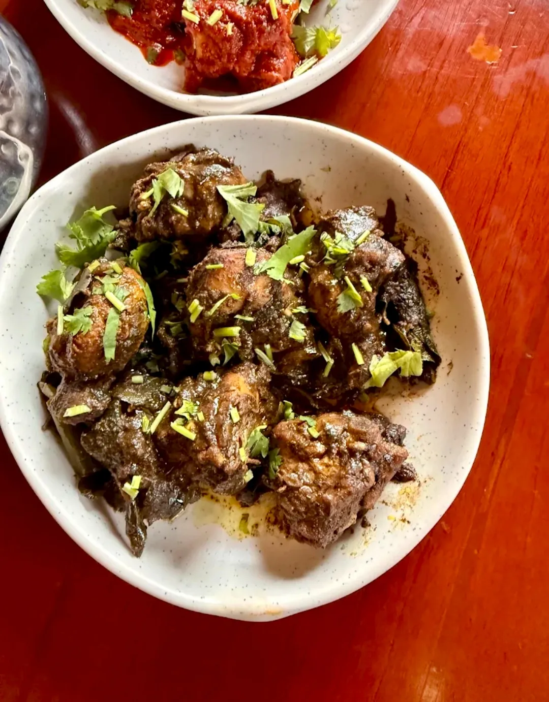 A bowl of dark, dry-fried meat with green chilli and coriander.